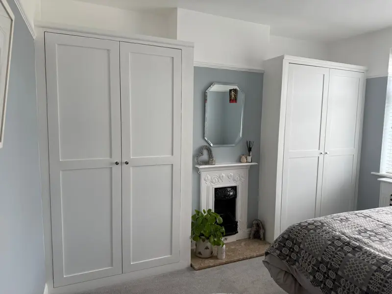 A matching pair of full-height white shaker alcove cupboards either side of a cast-iron bedroom fireplace